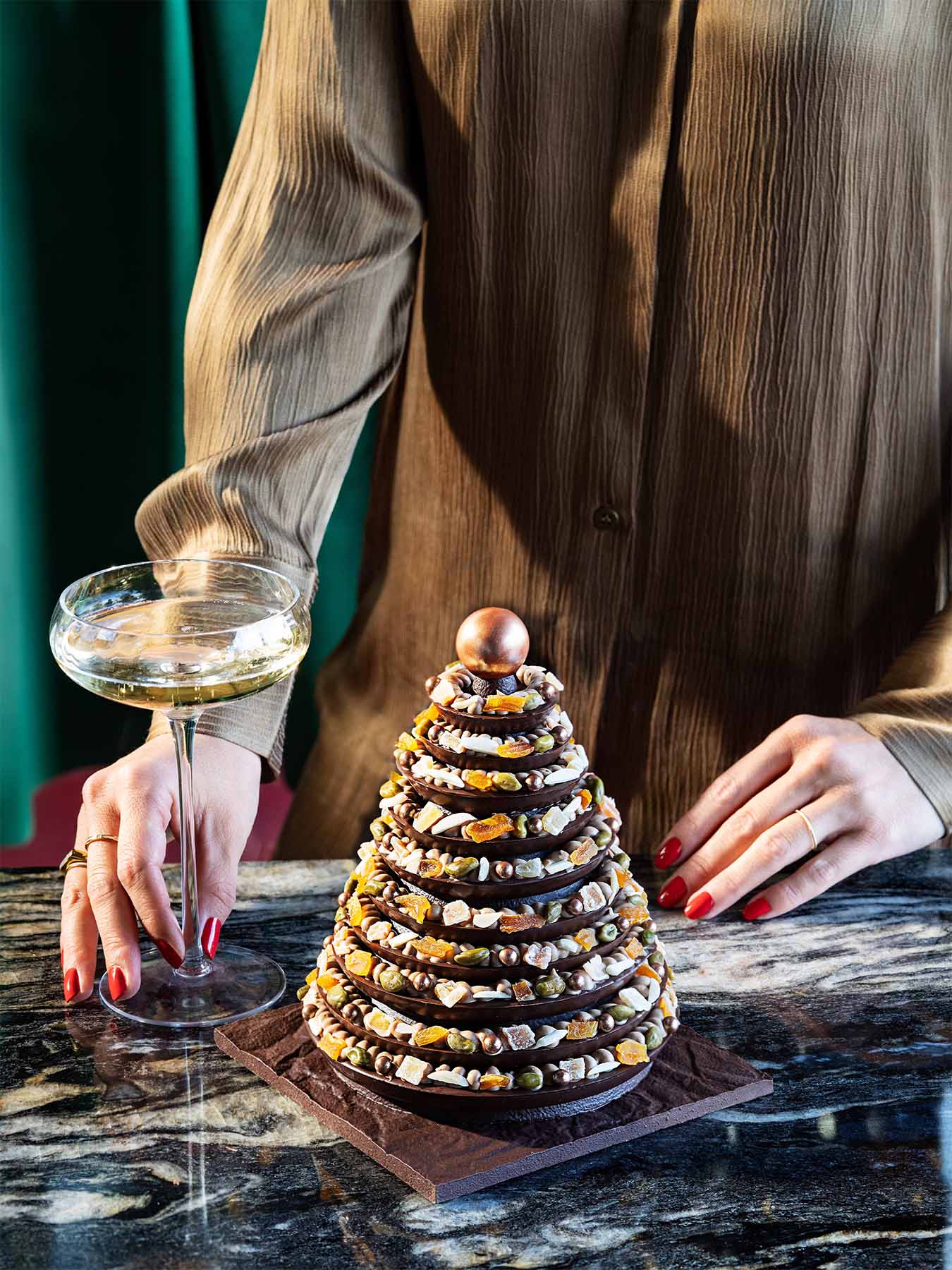 Eine Frau in festlicher Kleidung steht mit einem Glas Champagner vor einem etwa 20cm großen Schokoladen-Weihnachtsbaum
