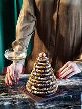 Eine Frau in festlicher Kleidung steht mit einem Glas Champagner vor einem etwa 20cm großen Schokoladen-Weihnachtsbaum